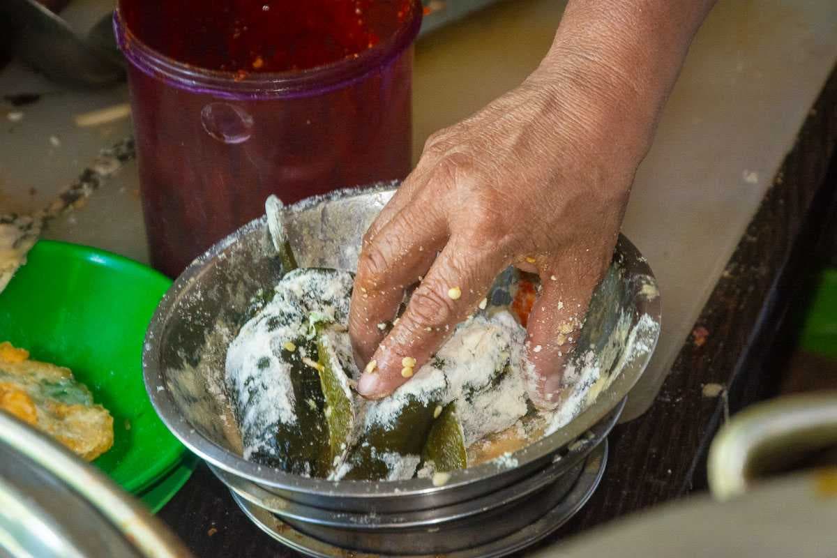 Silvia coats stuffed chiles with flour and eggs for chile rellenos.