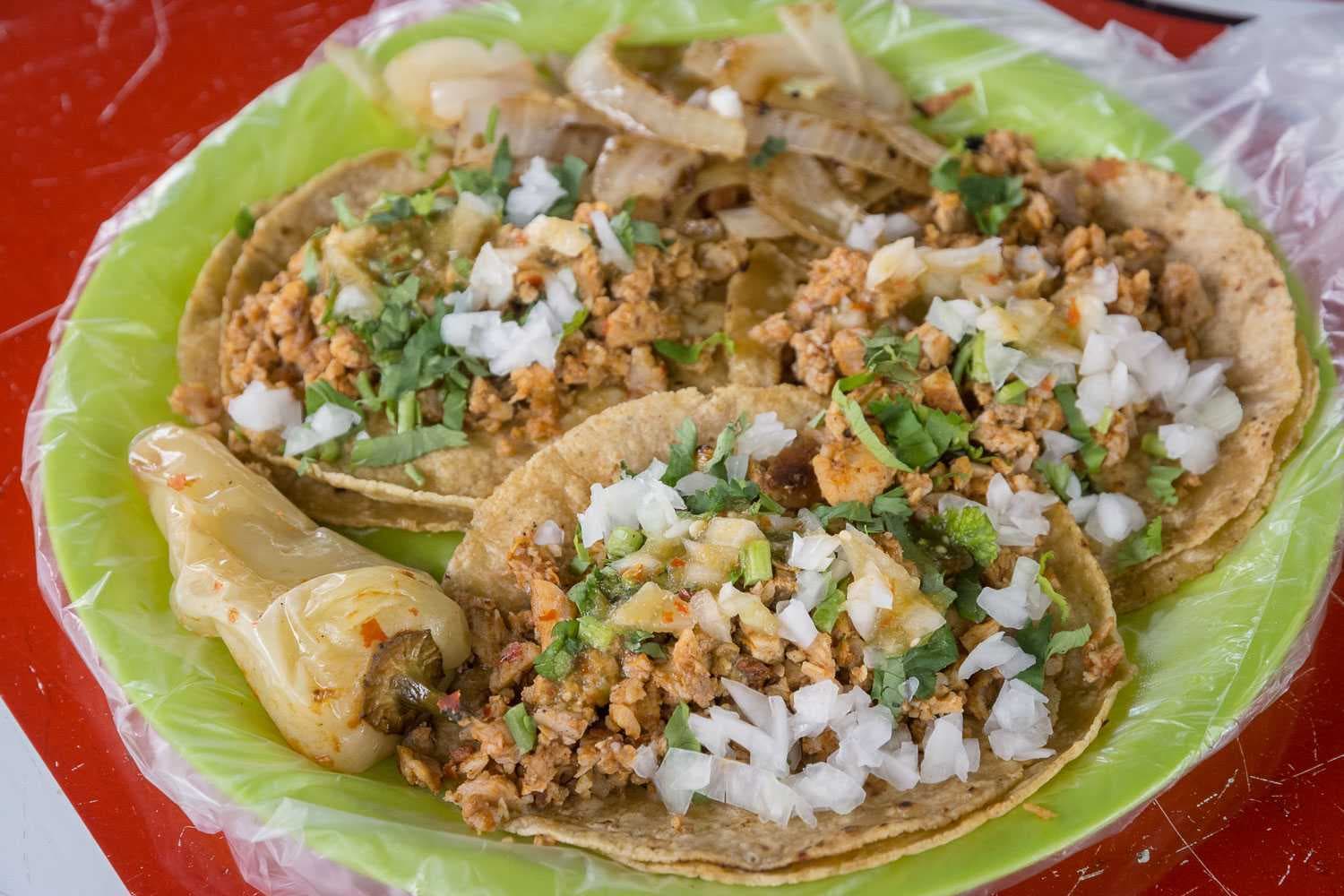 Sirven tacos de carne de res, chorizo, carnaza y cabeza de vaca. Estos son tacos adobada con chile güero y cebolla asada como acompañamiento.